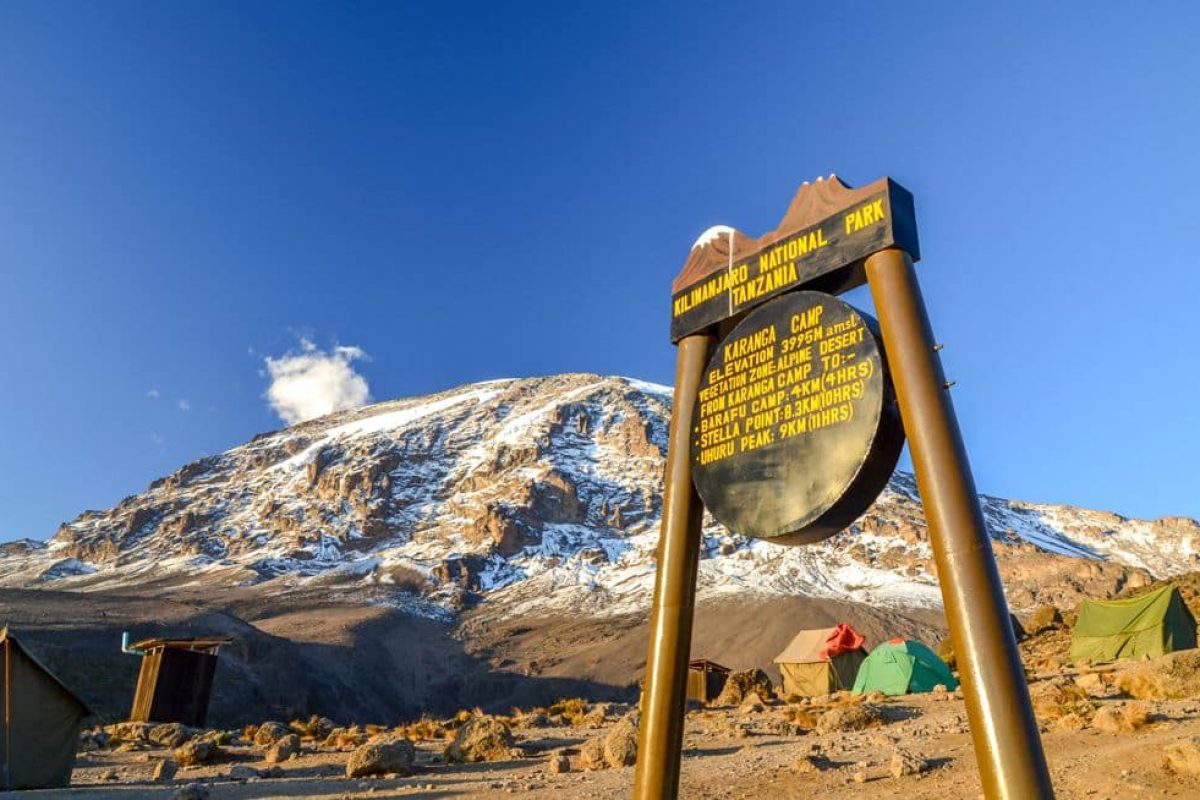 Karanga Camp at Mount Kilimanjaro – Tansania, Africa Kilimanjaro, Tanzania - March 9, 2015: Kibo with Uhuru Peak (5895m amsl) at Mount Kilimanjaro, Kilimanjaro National Park, seen from Karanga Camp at 3995m amsl. Park sign and tents in the background.